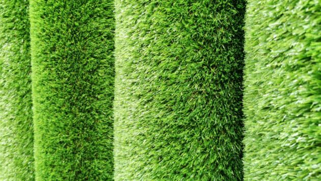 L'immagine mostra diversi rotoli di erba sintetica, accuratamente disposti uno accanto all'altro. Questi rotoli appaiono nuovi e di alta qualità, con fili di erba sintetica di un verde vivo e luminoso che emana un aspetto fresco e naturale. Ogni rotolo è avvolto strettamente, evidenziando la densità e l'uniformità dell'erba artificiale. La texture dell'erba è fine e regolare, con una lunghezza uniforme dei fili che suggerisce una superficie morbida e piacevole al tatto.