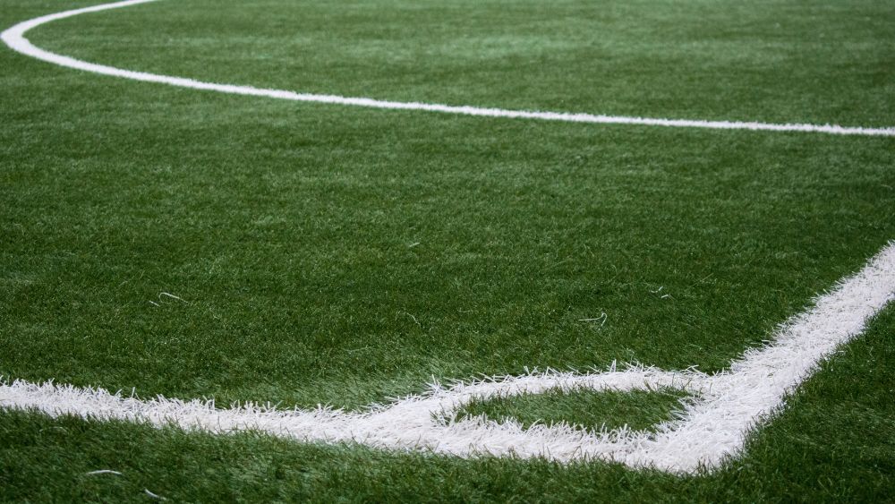 La foto mostra un dettaglio di un angolo di un campo da calcio in erba artificiale, conforme agli standard del FIFA Quality Programme, progettato per offrire qualità e prestazioni eccellenti. Questa superficie, certificata secondo le specifiche FIFA Basic e FIFA Quality Pro, garantisce uniformità di gioco e durabilità nel tempo. Ideale per competizioni professionistiche e amatoriali, rappresenta un esempio di eccellenza tra i campi da calcio in erba artificiale FIFA.