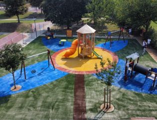 Vista del nuovo parco giochi a Lucca con pavimentazione antitrauma in erba sintetica colorata, giochi conformi alla normativa UNI EN 1176 e area ludica sicura per bambini.